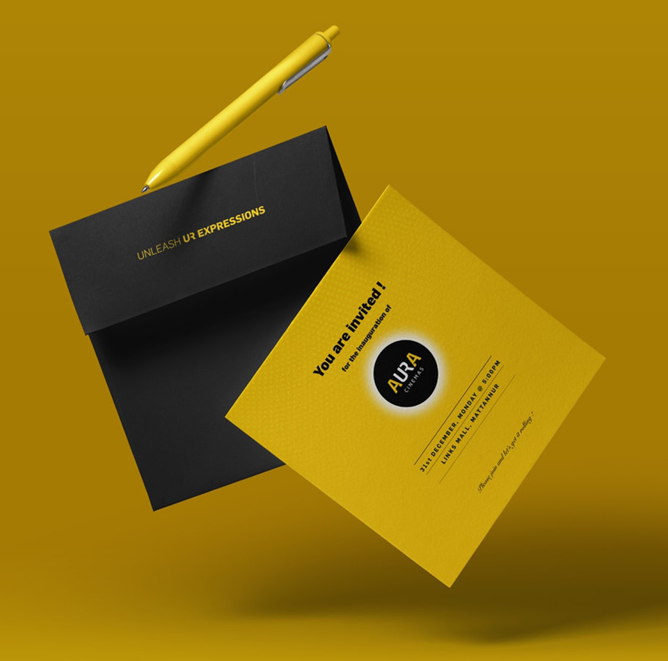 Corporate invitation for Aura Cinemas inauguration, featuring a yellow card, black envelope, and a stylish yellow pen.