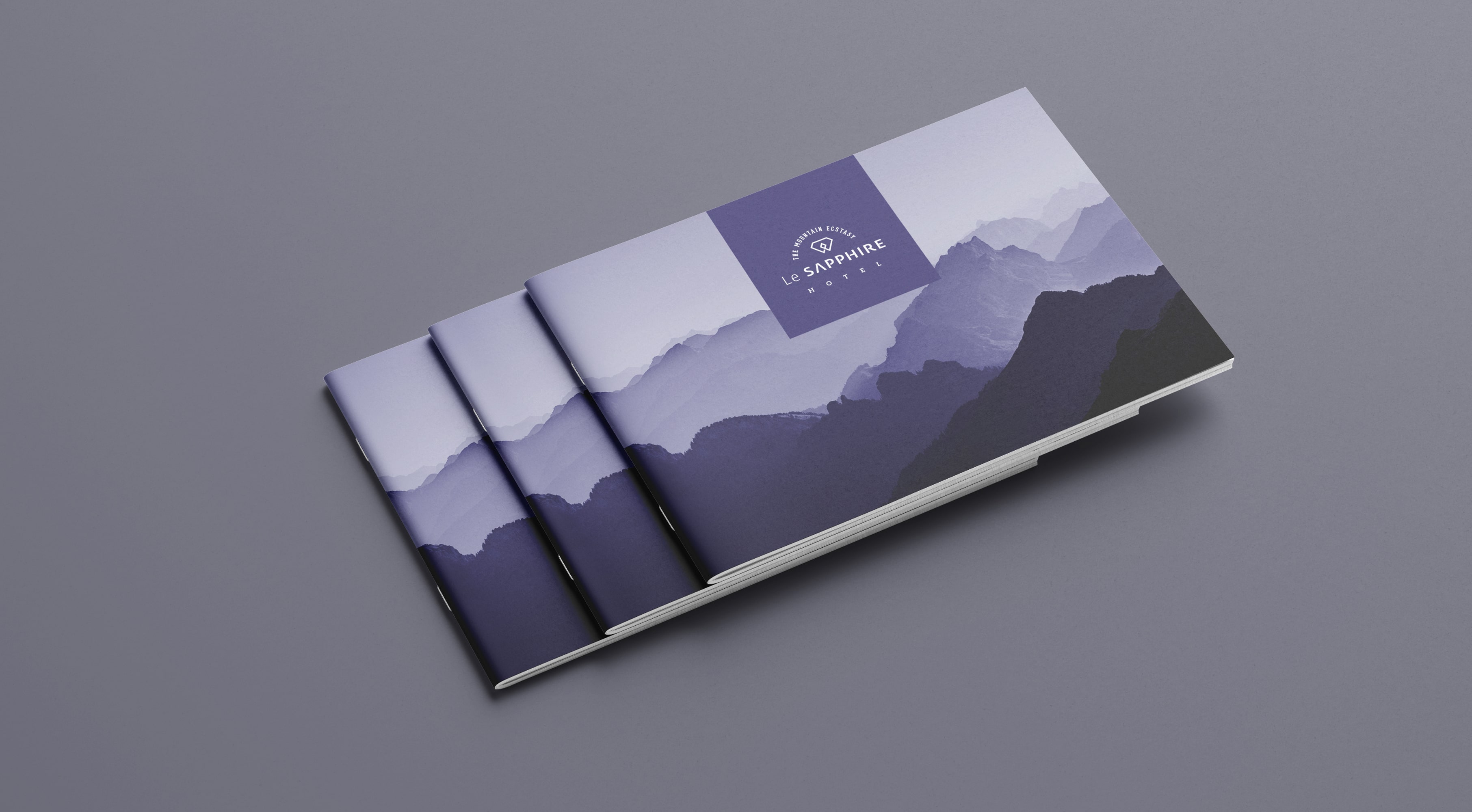 Le SAPPHIRE Hotel brochures with purple mountain landscape design and brand logo, stacked on a grey background.