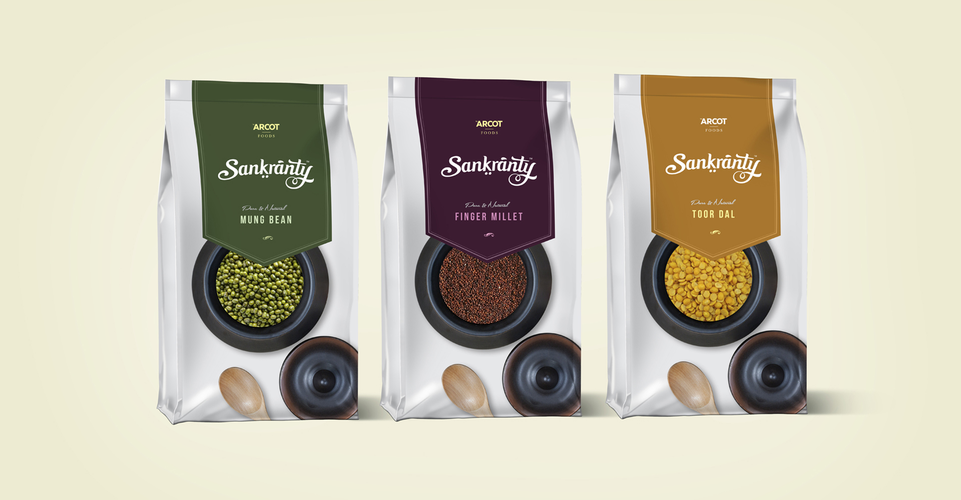 A trio of Sankranty branded packaging pouches for pulses: Mung Bean (green), Finger Millet (purple), and Toor Dal (orange). Each pouch features the brand logo, product name, and a window displaying the pulses inside.